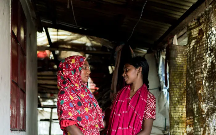 A woman and a girl stand facing each other in a doorway, holding hands, both smiling.